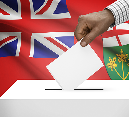 A hand dropping a ballot into a box with the Ontario flag in the background
